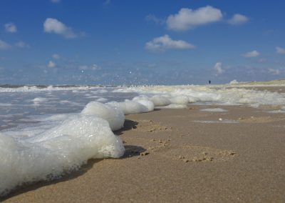 afgeblazen zee schuim op strand met in de verte een wandelaar na de storm in katwijk