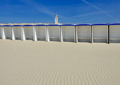 gerimpeld zand met lege houten tentjes voor de oude kerk van katwijk in de blauwe lucht