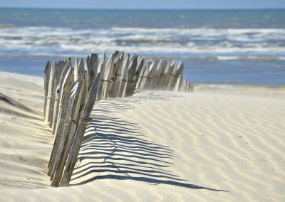 houten hek in gerimpeld zandstrand met stuivend zand en zicht op blauwe zee in katwijk