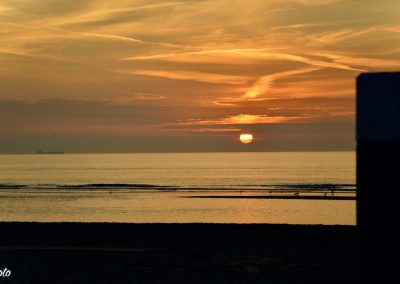 ondergaande zon in kleur oranje met op voorgrond strandpaal in katwijk aan zee