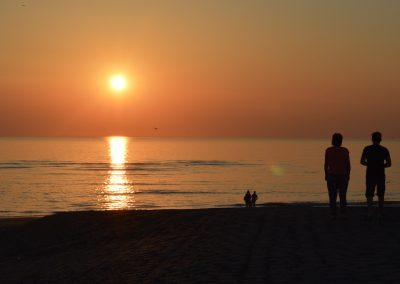 ondergaande zon met 2 paren in silhouet aan de waterkant van de zee in de kleur oranje