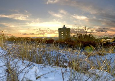 opgaande zon in besneeuwde duinen met zicht op watertoren van katwijk