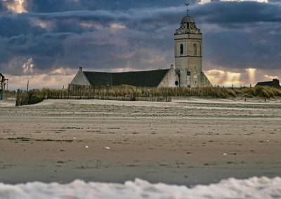 strand katwijk aan zee met zicht op dak en toren van oude kerk achter de duinen