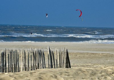 vier kitesurfers op stormachtige zee op strand houten hek in katwijk aan zee