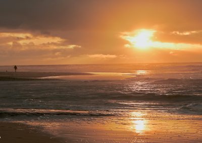 zonsondergang in gouden uur met glinsterende zee en in de verte een wandelende dame met hond